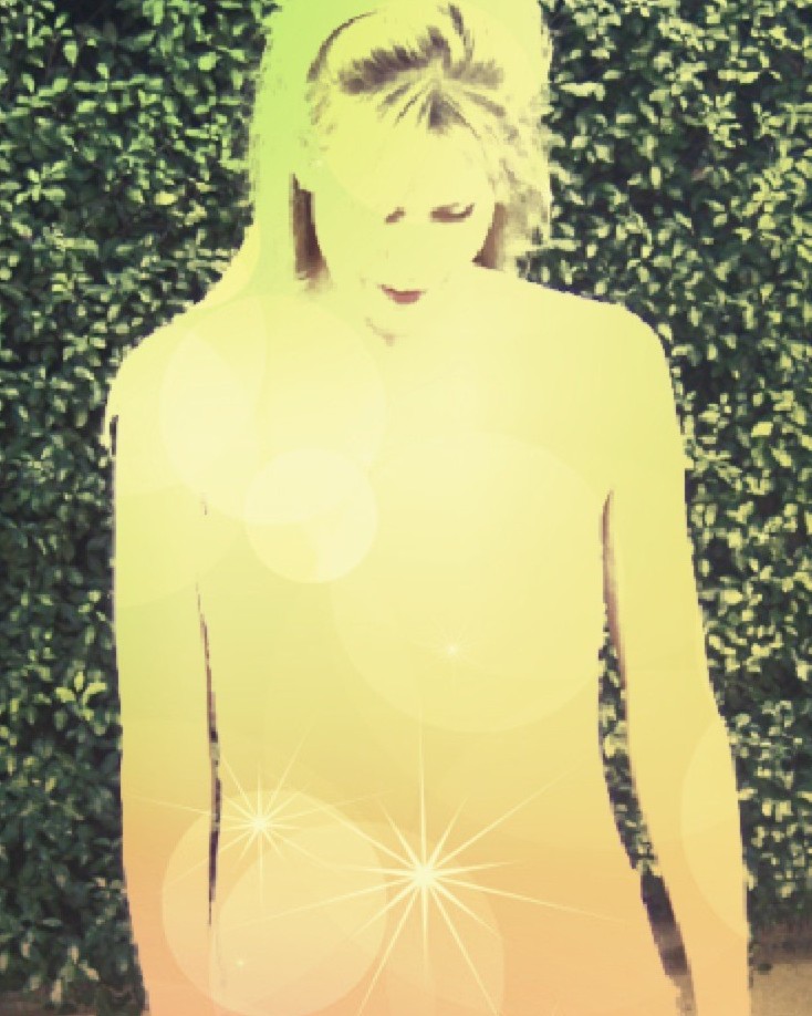 Jericho Jane in yellow light standing in front of green hedge with star on stomach
